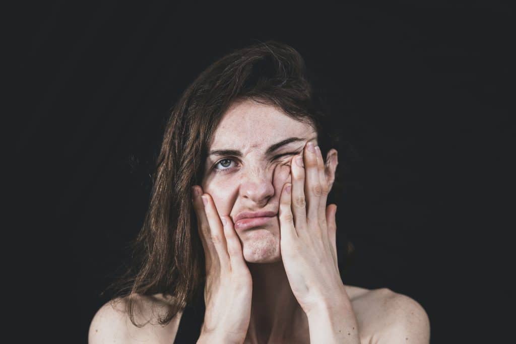 Une femme se tord le visage avec les mains, sur un fond noir.